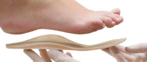 Gloved hand holding up a foot orthotic to the bottom of a foot